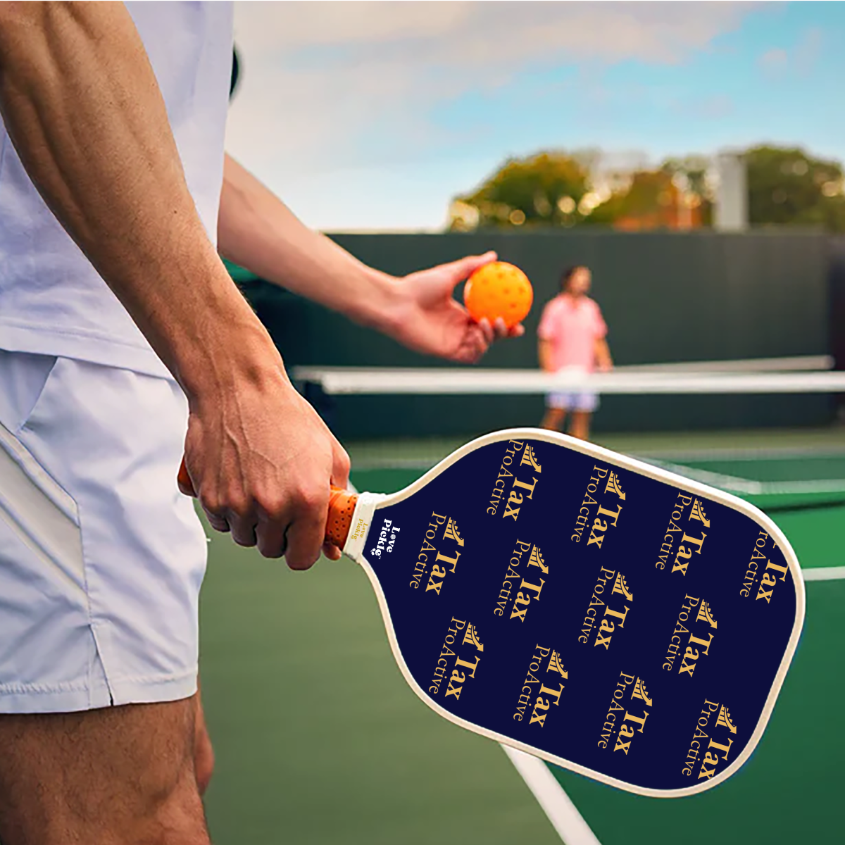 Hand holding the Love Pickle Custom Business Promo Branded Paddle and pickleball orange ball in a serving stance in a court